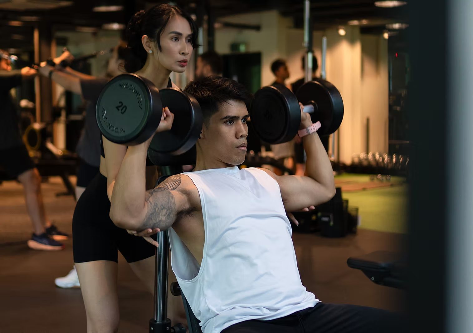 Two members pressing dumbbells overhead on the training floor at Rockwell Atletica.