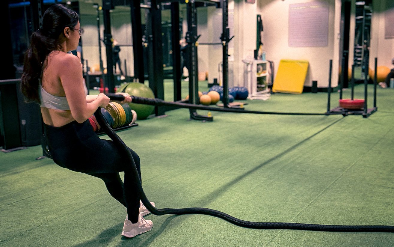 A member driving a rope pull across the turf of the Functional Zone at Rockwell Atletica.