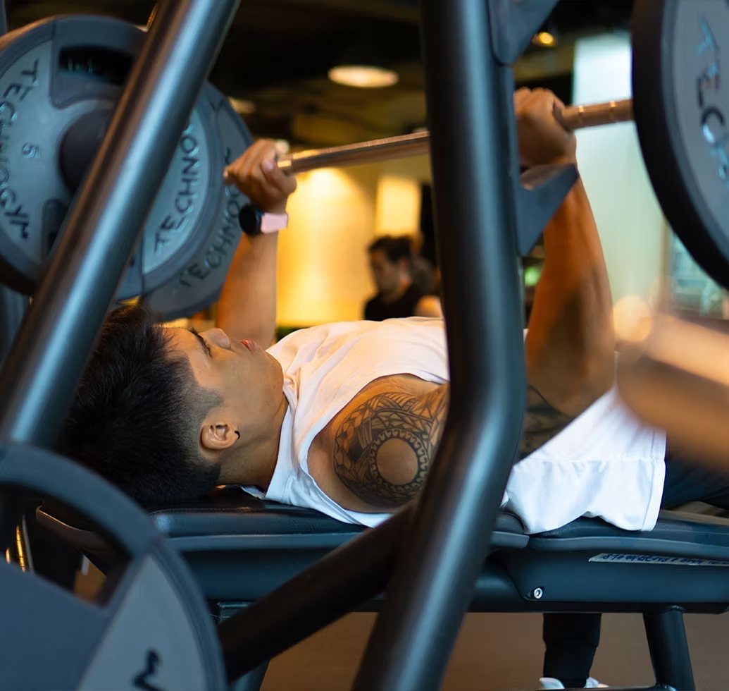 A member pressing a loaded Technogym barbell on the bench in the Lifting Floor.
