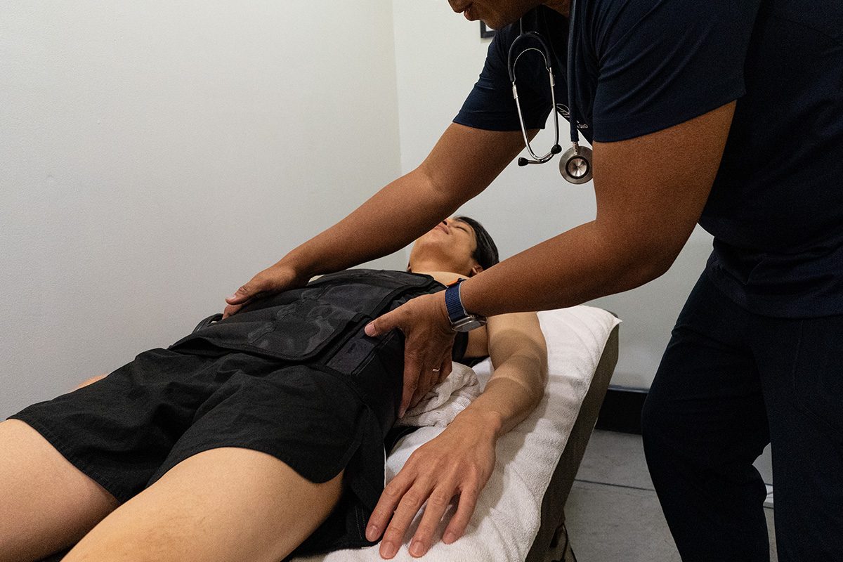 A doctor fitting a compression vest on a member lying on the treatment table.