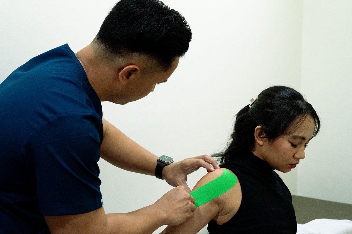A recovery team member applying kinesiology tape to a member's shoulder.
