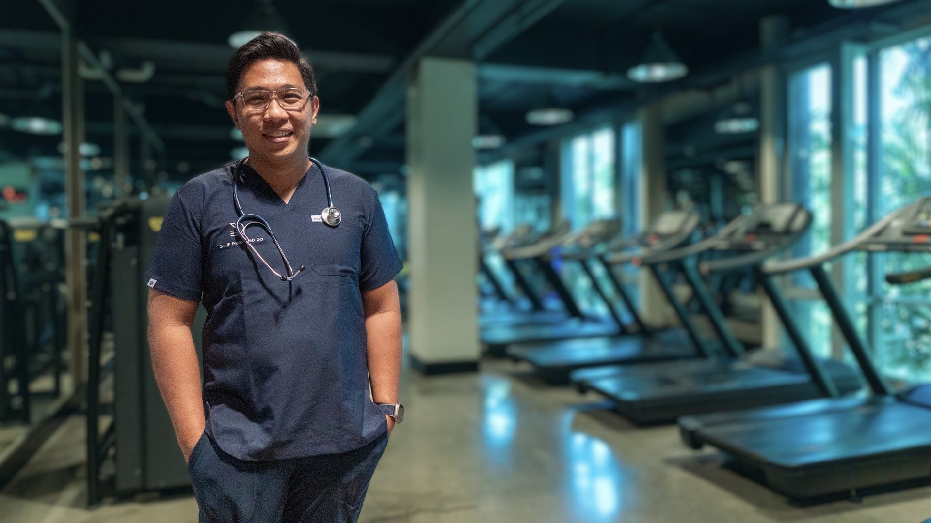 Dr. JP Prado of the Atletica recovery team standing on the training floor in scrubs.