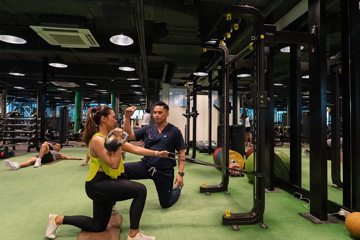 A recovery coach guiding a member through a kettlebell lunge with a resistance band on the training floor.